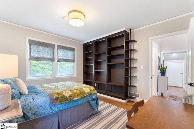 bedroom with wood finished floors, ornamental molding, and visible vents