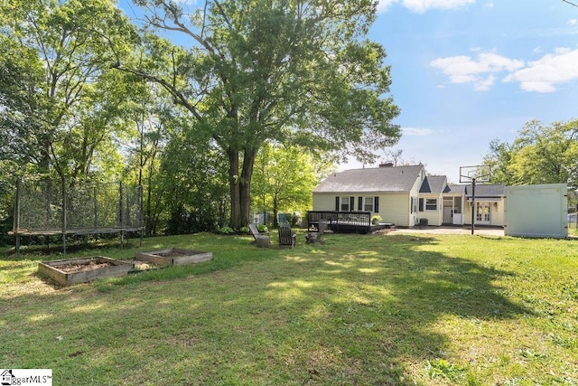 view of yard featuring a garden, a trampoline, and a deck