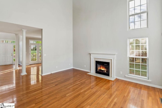 unfurnished living room featuring decorative columns, a fireplace with flush hearth, hardwood / wood-style flooring, and a high ceiling