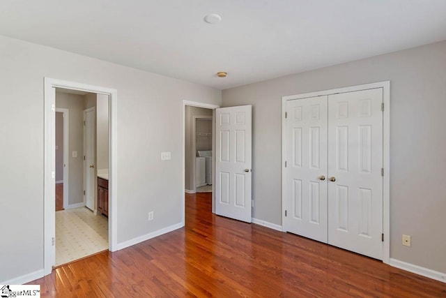 unfurnished bedroom featuring wood finished floors, baseboards, a closet, and washer / dryer