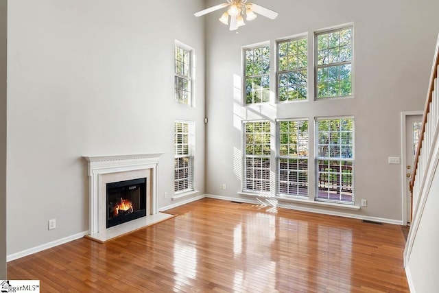 unfurnished living room with hardwood / wood-style flooring, a high ceiling, baseboards, and ceiling fan
