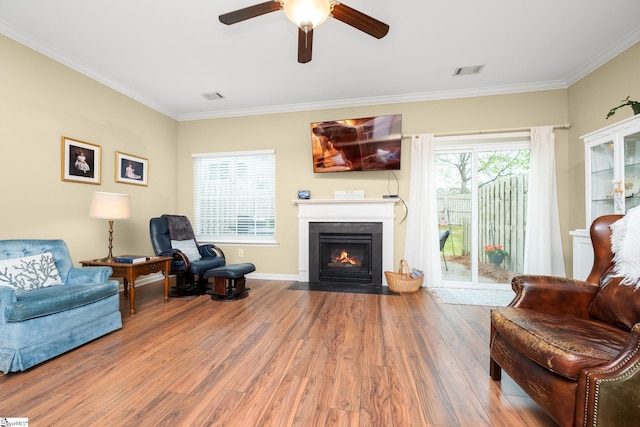living area featuring wood finished floors, ceiling fan, ornamental molding, and visible vents