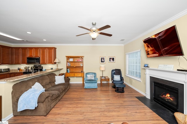 living room featuring baseboards, a ceiling fan, crown molding, a fireplace with flush hearth, and light wood-style floors