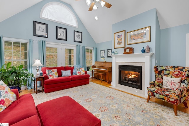 living area featuring a ceiling fan, a healthy amount of sunlight, wood finished floors, a fireplace with flush hearth, and high vaulted ceiling