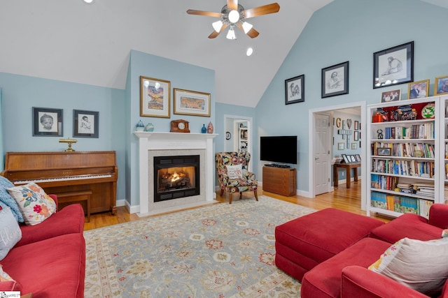 living area with ceiling fan, high vaulted ceiling, a fireplace with flush hearth, wood finished floors, and baseboards