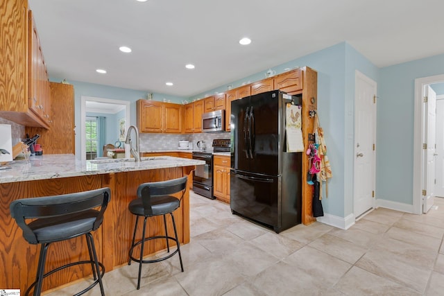 kitchen featuring a sink, a breakfast bar, a peninsula, black appliances, and decorative backsplash
