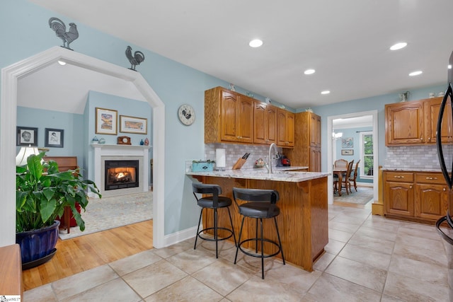 kitchen featuring backsplash, brown cabinetry, a breakfast bar, and a lit fireplace
