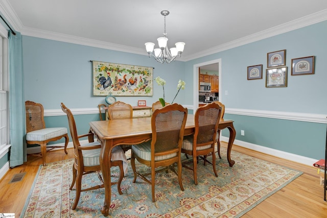 dining space with an inviting chandelier, light wood-style flooring, ornamental molding, visible vents, and baseboards