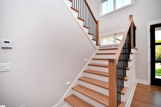 stairs featuring a towering ceiling, baseboards, and wood finished floors