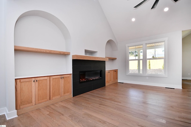 unfurnished living room featuring high vaulted ceiling, a glass covered fireplace, visible vents, light wood finished floors, and baseboards