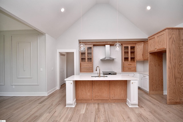 kitchen with wall chimney exhaust hood, glass insert cabinets, a kitchen island with sink, light countertops, and a sink