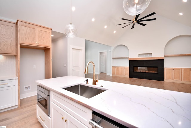 kitchen with a sink, light wood-type flooring, stainless steel microwave, recessed lighting, and light stone counters