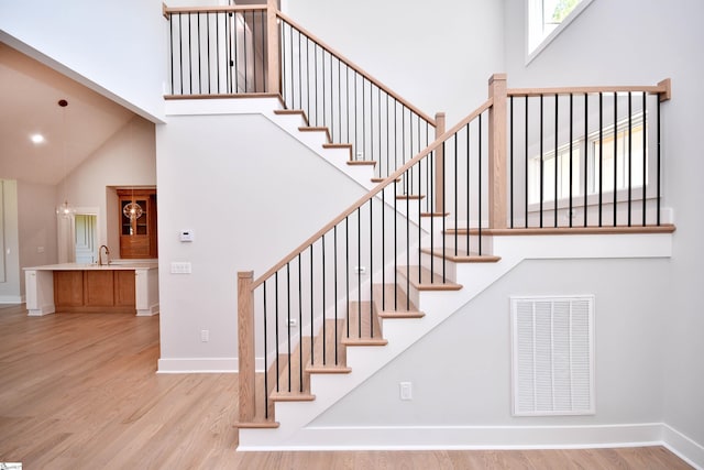 stairway with visible vents, baseboards, a high ceiling, and wood finished floors