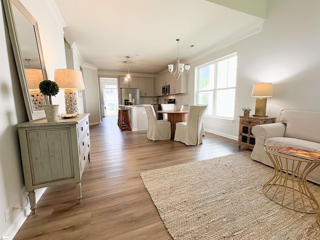 dining space with ornamental molding, a notable chandelier, light wood-style floors, and a healthy amount of sunlight