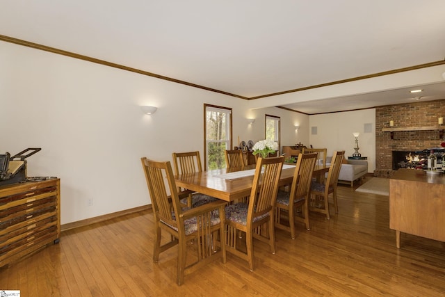 dining room featuring light wood-style floors, a fireplace, crown molding, and baseboards