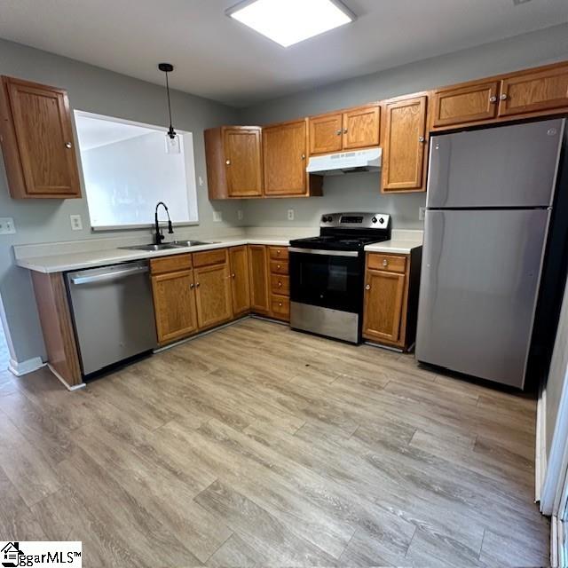 kitchen featuring under cabinet range hood, brown cabinets, a sink, and appliances with stainless steel finishes