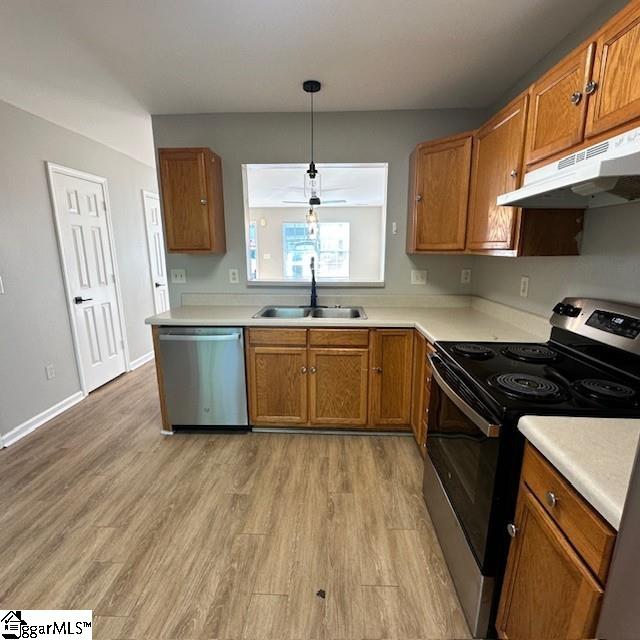 kitchen featuring under cabinet range hood, light wood-style floors, brown cabinetry, stainless steel appliances, and a sink