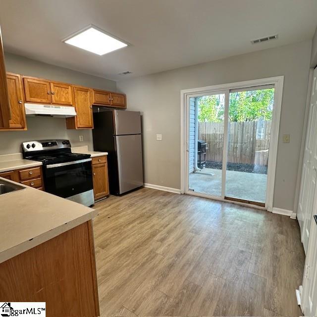 kitchen featuring light countertops, under cabinet range hood, visible vents, brown cabinetry, and appliances with stainless steel finishes