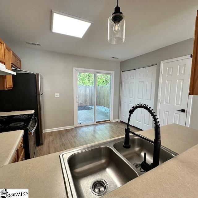 kitchen featuring light wood-style flooring, visible vents, a sink, range with electric stovetop, and brown cabinets
