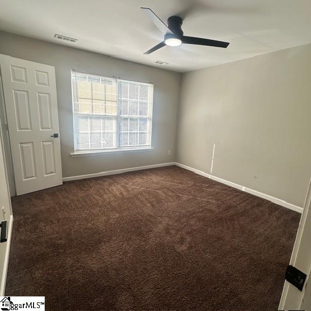 unfurnished room with dark carpet, ceiling fan, baseboards, and visible vents