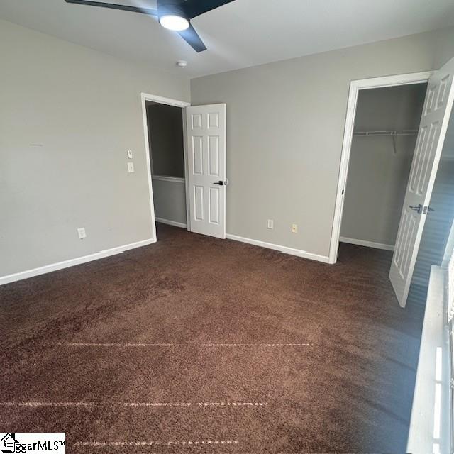 unfurnished bedroom with dark carpet, a closet, baseboards, and a ceiling fan