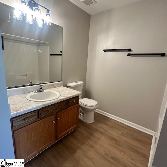 bathroom with vanity, toilet, wood finished floors, walk in shower, and baseboards