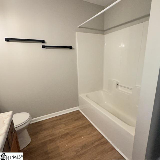 full bath featuring vanity, toilet, wood finished floors, washtub / shower combination, and baseboards