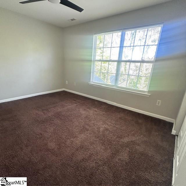 spare room featuring visible vents, ceiling fan, dark colored carpet, and baseboards