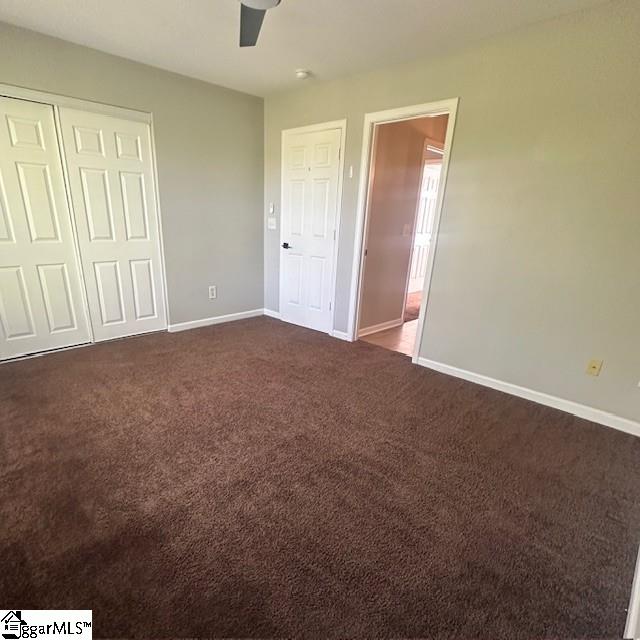 unfurnished bedroom with a closet, baseboards, a ceiling fan, and dark colored carpet