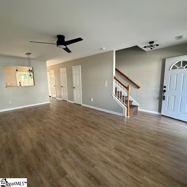 unfurnished living room featuring ceiling fan, visible vents, stairs, baseboards, and dark wood-style floors