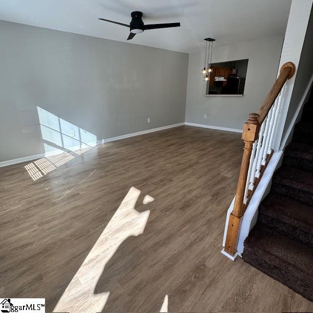 unfurnished living room featuring wood finished floors, baseboards, a ceiling fan, and stairs