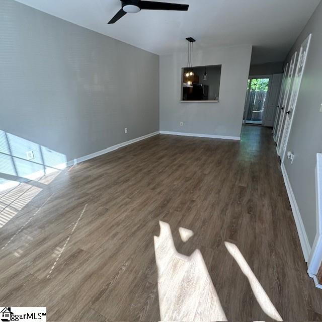 unfurnished living room featuring dark wood-style flooring, baseboards, and a ceiling fan