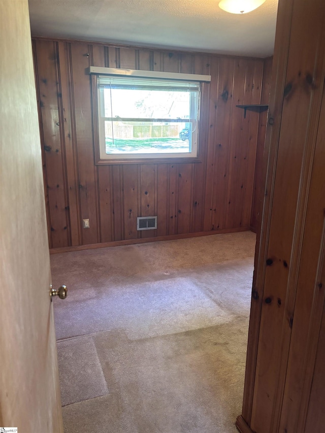 unfurnished room with wooden walls, visible vents, and carpet floors