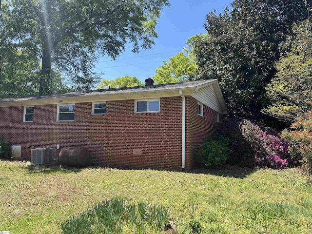 view of side of property with brick siding, central AC unit, a yard, and heating fuel