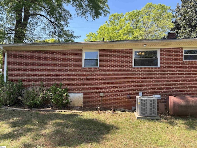 view of side of property featuring cooling unit, a yard, heating fuel, and brick siding