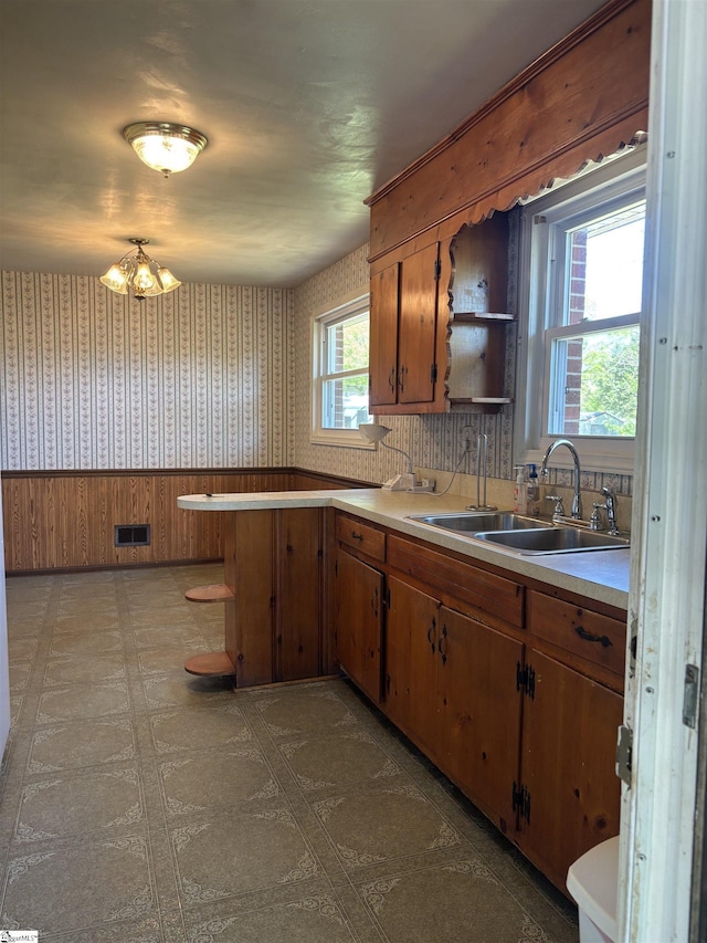 kitchen with wallpapered walls, light countertops, open shelves, brown cabinetry, and a sink