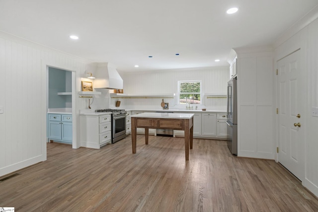 kitchen with light wood-type flooring, wall chimney range hood, open shelves, high end appliances, and visible vents