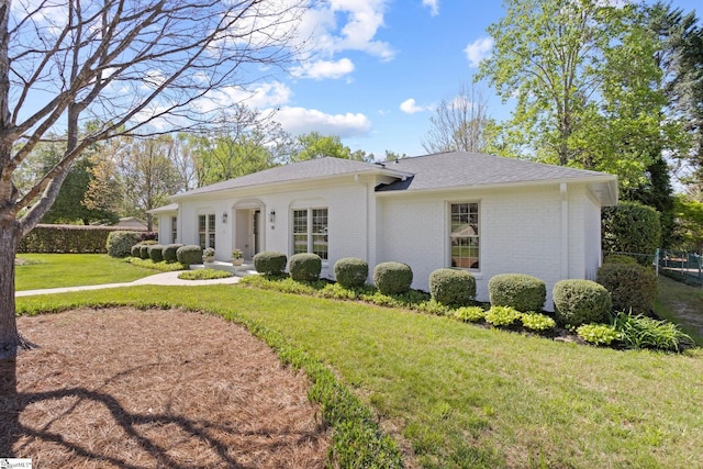 view of front facade featuring roof with shingles, fence, a front lawn, and brick siding