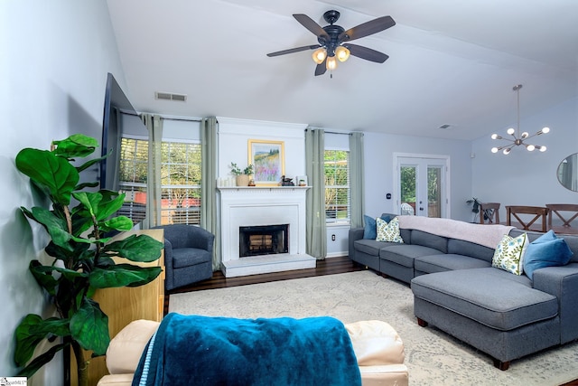 living room with wood finished floors, a fireplace with raised hearth, ceiling fan with notable chandelier, and visible vents