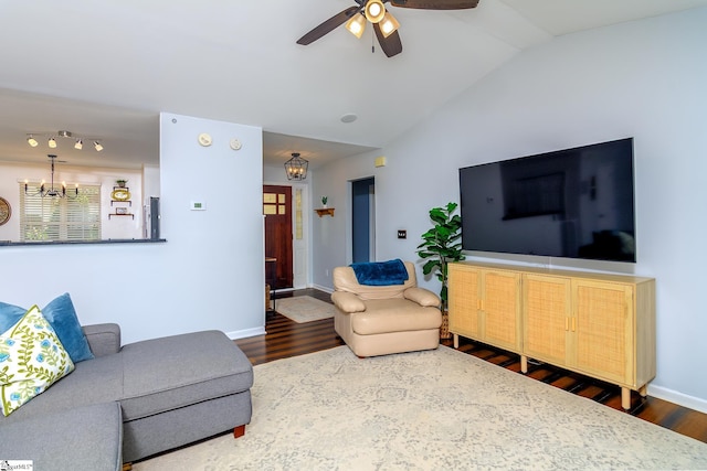 living room featuring baseboards, ceiling fan with notable chandelier, vaulted ceiling, and wood finished floors