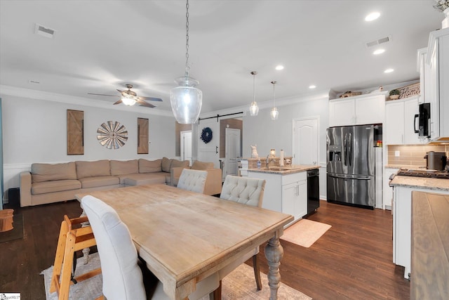 dining space featuring ornamental molding, a ceiling fan, a barn door, and dark wood finished floors