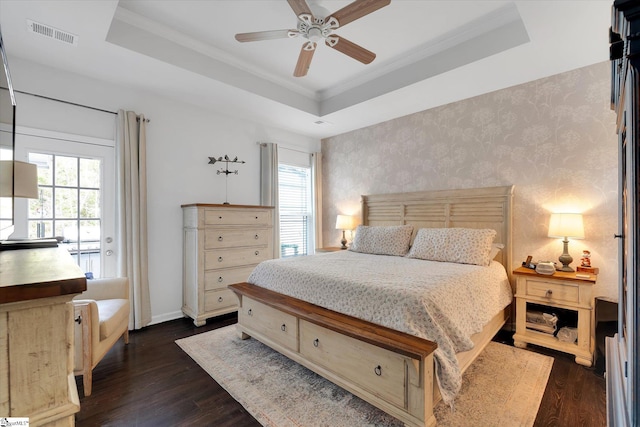 bedroom with dark wood-type flooring, multiple windows, a tray ceiling, and wallpapered walls