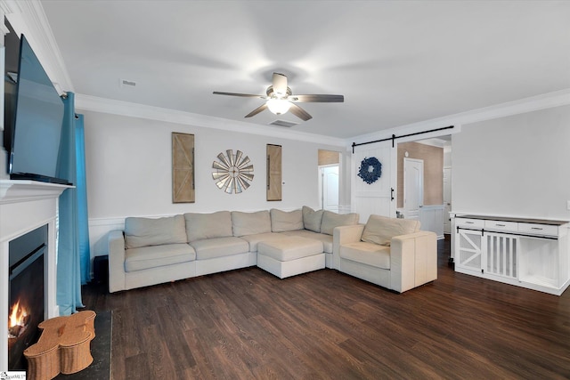living area featuring a lit fireplace, crown molding, ceiling fan, and a barn door