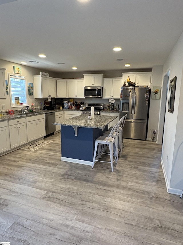 kitchen featuring dark stone countertops, a breakfast bar, stainless steel appliances, light wood finished floors, and a kitchen island