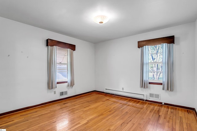 empty room with visible vents, a baseboard heating unit, baseboards, and light wood-style flooring