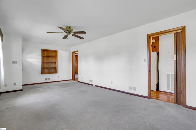 carpeted empty room with built in features, a ceiling fan, and visible vents