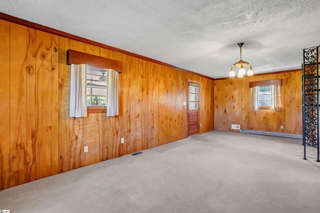 carpeted empty room with visible vents, a notable chandelier, baseboard heating, crown molding, and wood walls