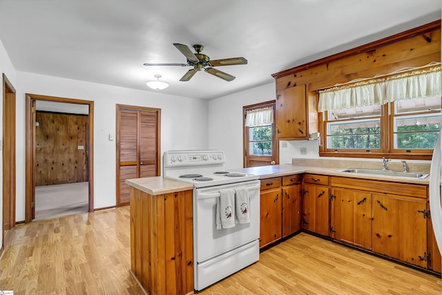 kitchen featuring white range with electric stovetop, a sink, light countertops, a peninsula, and light wood finished floors