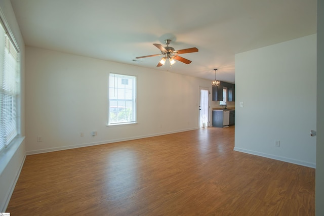 empty room with a sink, baseboards, wood finished floors, and ceiling fan with notable chandelier