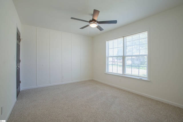 carpeted spare room featuring baseboards and a ceiling fan